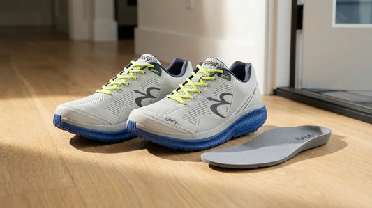 A pair of G-Defy Mighty Walk walking shoes on a wood floor with one removable insole lying beside them