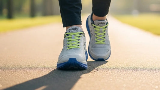 Active adult mid-stride on a sunlit path wearing gray and blue G-Defy Mighty Walk cushioned walking shoes