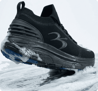 Black athletic shoe with blue sole accents, sock-like ankle, being cleaned on a foamy surface.
