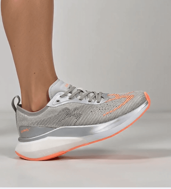 Running shoe in grey mesh with orange accents, white and silver midsole, and orange outsole, worn on a foot.