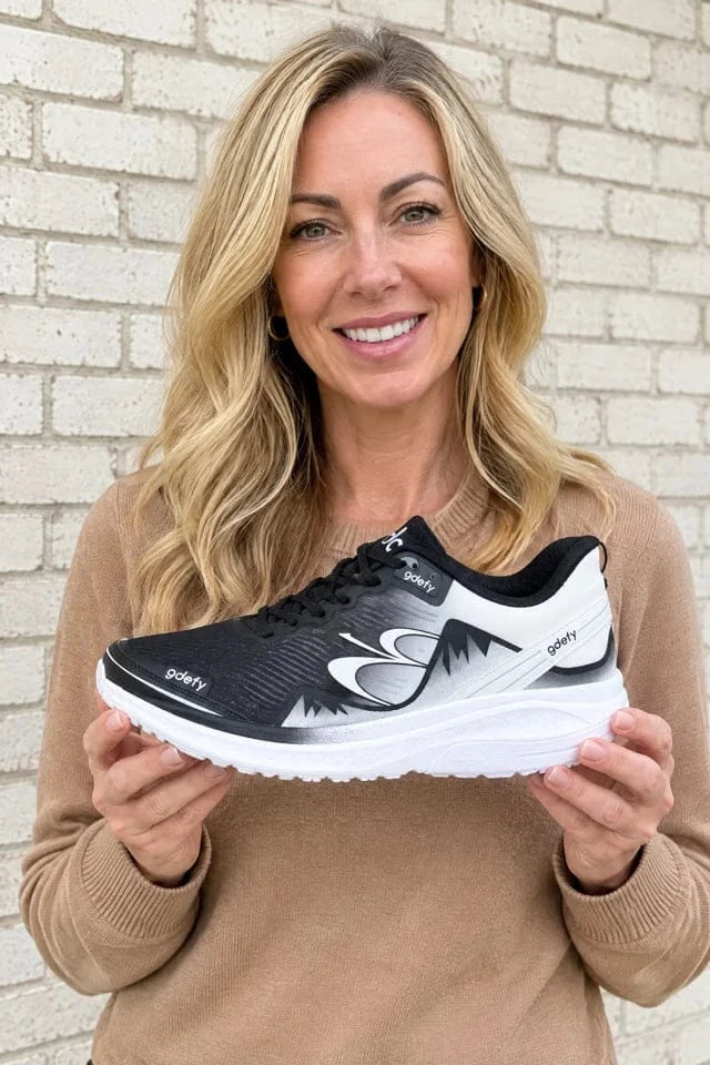 Illustrative portrait of a woman holding a GDEFY shoe beside a pale brick wall
